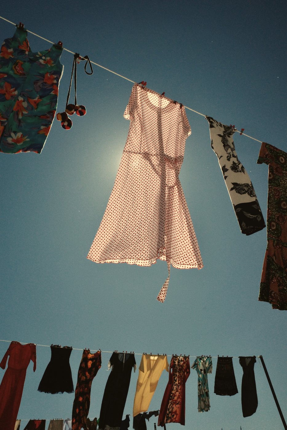 Vestidos diferentes pendurados em varais contra o céu, um deles atravessado pela luz